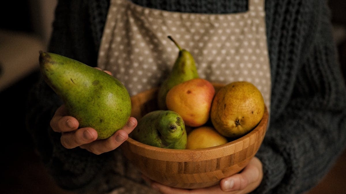 Rustic image of hands holding a wooden bowl filled with pears, showcasing warmth and freshness.