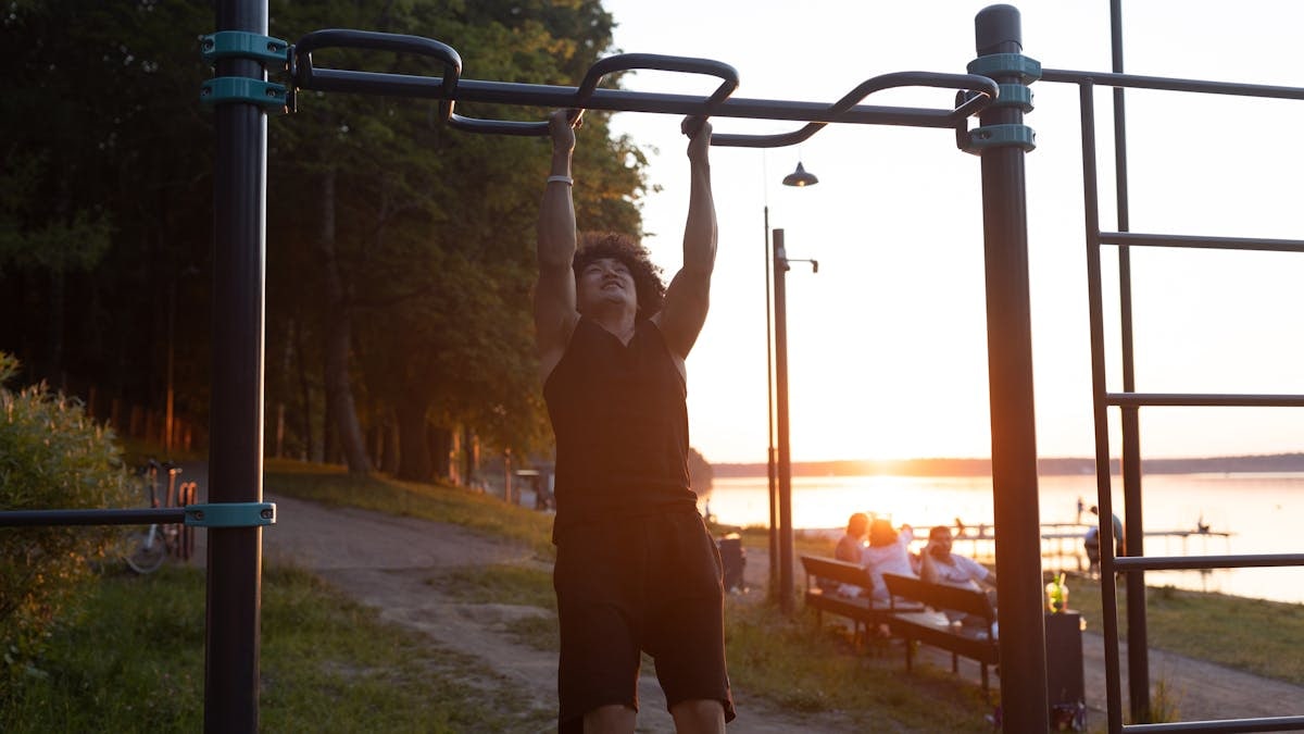 A man working out on pull-up bars in a park during sunset, capturing a healthy and active lifestyle.